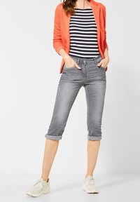 Jeans cortos grises con puños enrollados, bolsillos frontales y cierre de botón, combinados con una camisa a rayas y una blazer naranja. Zapatillas blancas.