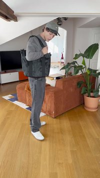 Čierna taška na rameno s textúrovanou látkou, dlhými popruhmi a obdĺžnikovým tvarom, nosená cez šedý sveter a svetlo šedé džínsy.