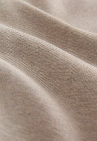 Prim-plan cu material tricotat bej deschis, ce arată o textură moale și un model fin cu nervuri și pliuri delicate.