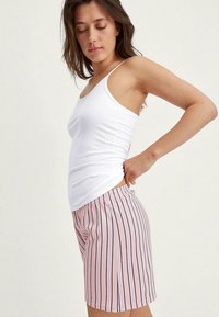 Lichte witte tanktop gecombineerd met roze shorts met verticale marineblauwe strepen. De shorts hebben een elastische tailleband en een losse pasvorm.