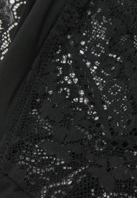 Tela de encaje negra con intrincados patrones florales, combinada con material negro liso. Detalle textural con finos tejidos abiertos y secciones sólidas.