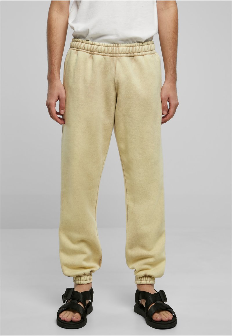 Lys beige joggebukser med elastisk midjebånd og mansjetter. Laget av mykt stoff, med en avslappet passform og side-lommer. Brukt med svarte sandaler.