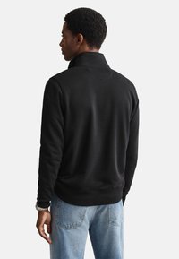 Felpa nera con collo alto, texture morbida, polsini e orlo a coste, indossata con jeans di denim chiaro blu.