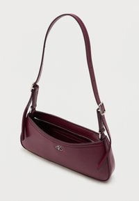 Bordowa skórzana torebka na ramię o smukłym, zakrzywionym kształcie. Posiada zamykaną na zamek komorę, regulowany pasek oraz srebrny akcent z logo.