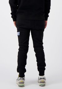 Zwarte sweatpants met een slim fit ontwerp, voorzien van een zijzak met een lichtblauwe accenten, aangevuld met grijze en gele sportschoenen.