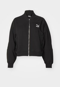 Chaqueta corta negra hecha de tela suave, con cuello alto, cierre frontal con cremallera y puños elásticos. Presenta un logo blanco de Puma en el pecho.