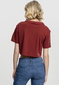 Forkortet rustfarvet t-shirt i blødt bomuld med korte ærmer og afslappet neckline, parret med højtaljede blå jeans.