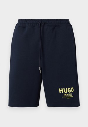 Marineblå shorts med snøre og elastik i taljen samt gul tekst "HUGO MCMXCIII Registered Trademark" på det nederste venstre ben.