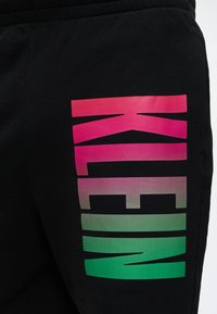 Tissu noir avec un grand texte vertical "KLEIN" en dégradé de couleurs allant du rose en haut au vert en bas.