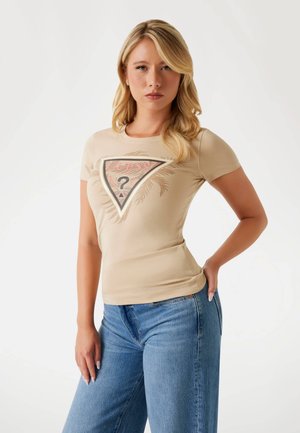 T-shirt ajusté beige à manches courtes, avec un design graphique triangulaire et du texte en rose et noir. Associé à un jean bleu clair.