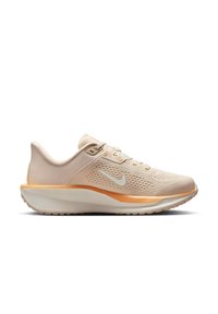 Zapatilla de correr de color beige claro con parte superior de malla transpirable, media suela naranja y swoosh blanco de Nike. Presenta un diseño texturizado y un collar acolchado.