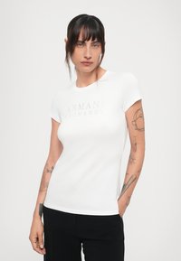 Wit aansluitend T-shirt met korte mouwen, voorzien van een glanzend grijze "ARMANI EXCHANGE" logo op de borst. Zachte katoen stof.