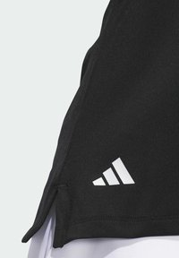 T-shirt de sport noir avec fentes latérales, fabriqué en tissu extensible. Il présente un logo Adidas blanc en bas à gauche et des coutures plates.