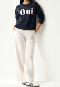 Pull en maille bleu marine avec graphisme "Oui" et détail cœur rouge, associé à un pantalon large crème et des baskets blanches avec des rayures noires.