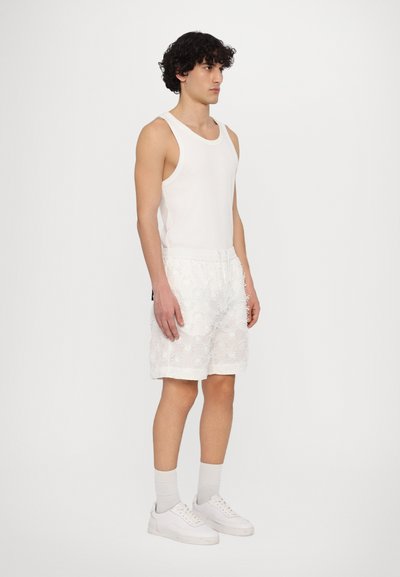 Hvid tanktop parret med knælange shorts med et blomsterbroderet mønster. Båret med hvide sneakers og lysegrå sokker.