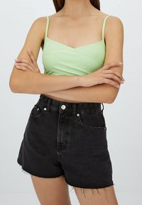 Vaaleanvihreä spagettihihnainen toppi ja mustat korkeavyötäröiset farkkushortsit, joissa on rispaantuneet reunat, etutaskut ja metallinen nappikiinnitys.