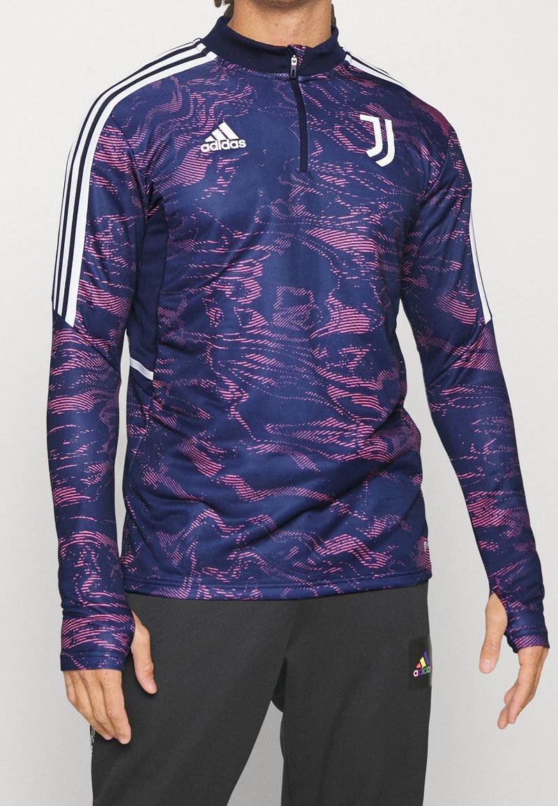 Pitkähihainen tummansininen urheilupaita, jossa on vaaleanpunainen kuvio, neljännesvetoketjullinen kaulus ja valkoiset Adidas- sekä Juventus-logot; sileä, joustava kangas mukavuutta varten.