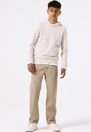 Lichtbeige hoodie met de tekst "REALITY" op de borst, gecombineerd met lichtbruine jeans en witte sneakers. Eenvoudig ontwerp en casual fit.