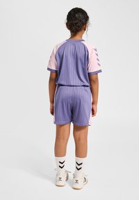 Sportoutfit i lila och rosa med smala ränder, kortärmad tröja och shorts med elastisk midja, kombinerat med vita strumpor med svarta chevrons.