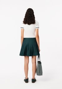  Haut blanc à manches courtes avec des accents noirs, associé à une jupe plissée verte. La tenue comprend des chaussures noires à lacets et un sac fourre-tout à motifs.