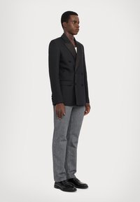 Svart dubbelknäppt blazer med satinrevers, matchad med grå raka jeans och svarta läderskor. Enkel, skräddarsydd design.