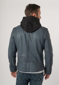 Blauwe leren jas met een zwarte, gebreide capuchon. Kenmerken zijn onder andere zichtbare stiksels en zijzakken, gecombineerd met spijkerbroek.