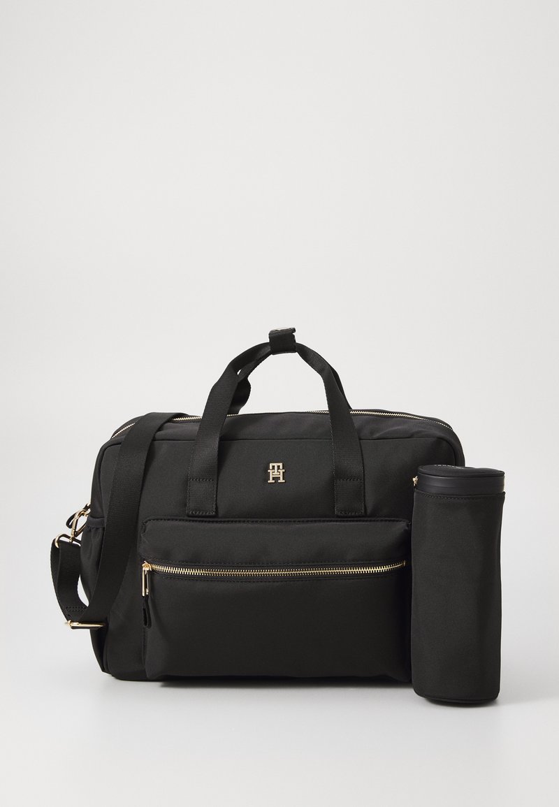 Sac de voyage noir en tissu durable, avec des accents de zip dorés, des poignées doubles, une bandoulière détachable et un étui cylindrique assorti.