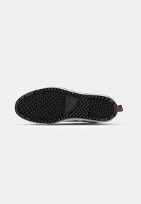 Rubber sneaker sole with a textured black bottom, featuring a zigzag pattern and a khaki detailing at the heel. White midsole accent.