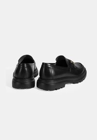 Schwarze Lederschuhe mit glatter Oberfläche, runder Zehenpartie und dicker Gummisohle; mit einem Slipper-Design und minimalistischen Akzenten.