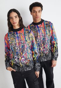 Fargerik sweatshirt med intrikate mønstre i livlige rosa, blå, gul og svart, med elastiske mansjetter og kant.