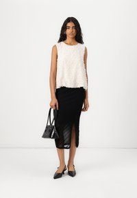 White sleeveless top with textured fabric, paired with a black ribbed skirt featuring a side slit, black handbag, and pointed shoes.