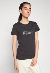 Camiseta de algodón negra con un logo de Puma texturizado y reflectante en el centro. Manga corta y escote redondo clásico. Tela suave.