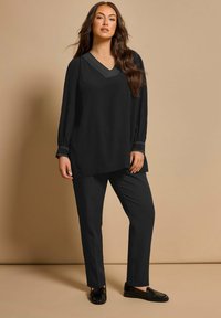 Tunica nera con scollo a V e cuciture a contrasto, abbinata a pantaloni e scarpe neri. Tessuto morbido, vestibilità rilassata, maniche lunghe.