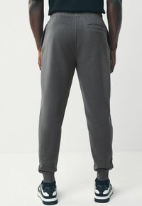 Gray joggers with a smooth texture, elastic waistband, side pockets, and ribbed cuffs. Worn with black and white athletic shoes.