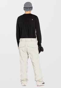 Camisa negra de manga larga para hombre combinada con pantalones de nieve beige. El gorro presenta rayas horizontales en blanco y negro con acentos de logotipo.