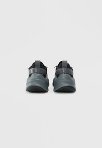 Sorte svarte og grå treningssko med et glatt, avrundet design, som har en teksturert såle, elastiske stropper og en forsterket hæl.