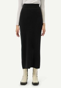 Jupe noire en tricot côtelé, longueur midi longue, taille haute, motif texturé. Associée à des bottines crème à la cheville avec des accents noirs.