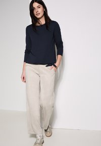 Maglietta a maniche lunghe di colore blu navy abbinata a pantaloni a gamba larga beige chiaro, caratterizzati da una texture morbida e tasche laterali. Completa con sneakers grigie.