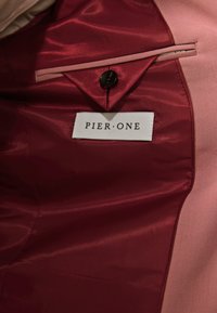 Roter Satin-Innenraum mit einem rosa Futter, ausgestattet mit einem Knopf und einem Etikett, das "PIER ONE" liest. Die Oberfläche ist glatt und glänzend.
