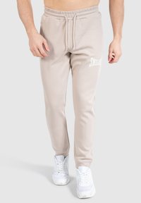 Beige joggerbukser med snoretræk i taljen, sidelommer og hvidt logoaccent. Fremstillet af blødt stof med et tapered leg-design.