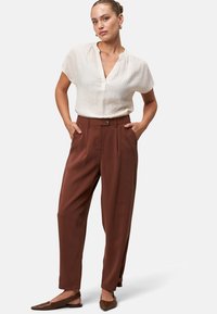 Blusa bianca a maniche corte con texture e scollo a V, abbinata a pantaloni a gamba larga marroni a vita alta e ballerine marroni a punta.