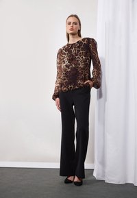 Blouse à imprimé léopard à manches longues avec encolure froncée, associée à un pantalon noir à jambe droite et des chaussures noires. Design simple et élégant.