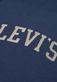 Mörkblått tyg med upphöjda silverbokstäver som står "LEVI'S." Tyget har en slät, strukturerad yta.