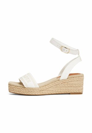 Sandalias de cuña con correas de tela blanca, una correa en el tobillo con herrajes dorados y una suela de plataforma de yute trenzado. Plantilla texturizada en un tono neutro.