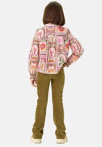 Veste colorée à motifs avec des cœurs et des plantes, associée à un pantalon en velours côtelé vert olive texturé et des chaussures de couleur claire.