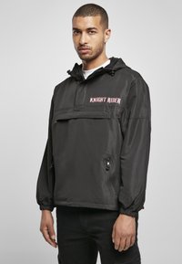 Muste must jacket, millel kapuuts, esikott, elastsed mansetid ja "KNIGHT RIDER" tekst roosas toonis. Sile tekstuur ja minimalistlik disain.