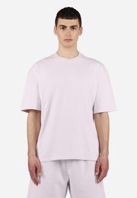 T-shirt surdimensionné rose clair avec des manches courtes, col rond et un logo discret sur la poitrine. Tissu en coton doux et coupe décontractée.