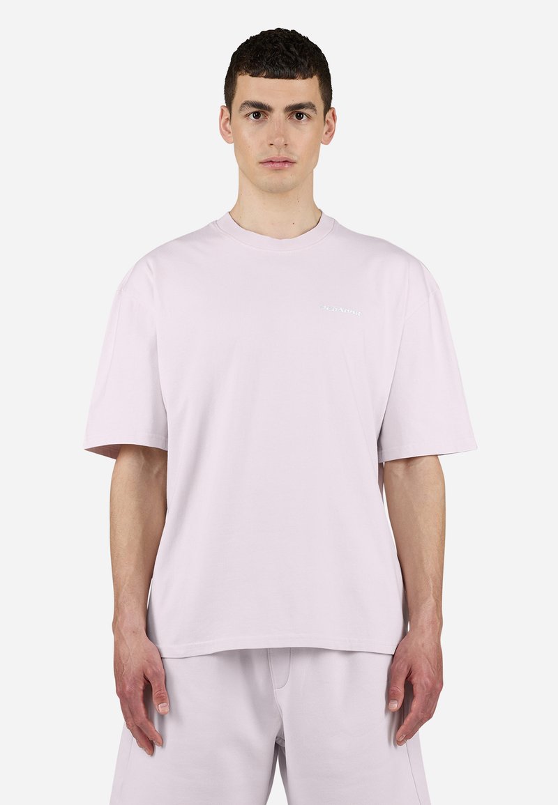 T-shirt surdimensionné rose clair avec des manches courtes, col rond et un logo discret sur la poitrine. Tissu en coton doux et coupe décontractée.