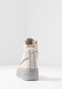 Beige-kankaiset korkeavartiset tennarit harmaalla kumipohjalla, joissa on takakiinnitysvetoketju ja joustavat nauhat. Pintakuviointi ja sivuviiva.