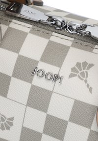Primo piano di un tessuto a quadri grigio e bianco con una cerniera argentata e il logo "JOOP!" su una superficie testurizzata.